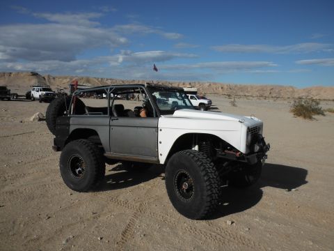 1979 Ford Bronco - A heavily modified Ford Bronco sits in a desert area with other vehicles in the background under a partly cloudy sky.