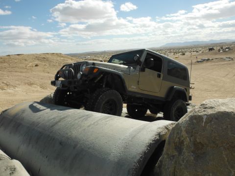 1979 Ford Bronco - Jeep Wrangler Rubicon navigates concrete obstacles in a desert off-road park.