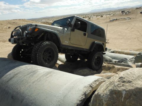 1979 Ford Bronco - A tan Jeep Wrangler Rubicon navigates a rocky, off-road course with large concrete pipes.