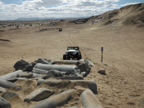 1979 Ford Bronco - A white 1979 Ford Bronco navigates sandy terrain, with other vehicles visible in the vast desert landscape.