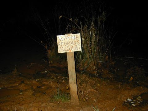 1996 Ford Bronco - A wooden sign marks Wayne Redman's Mud Hole, set against a dark, muddy background with tall grass.