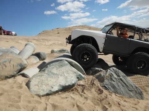 1979 Ford Bronco - A modified off-road vehicle with a roll cage is driven over large rocks in a desert landscape.