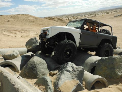 1979 Ford Bronco - A modified off-road vehicle navigates a rocky and pipe-filled terrain under a bright sky.