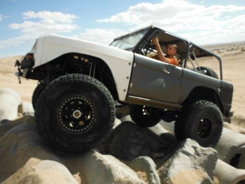 1979 Ford Bronco - A heavily modified off-road vehicle navigates a rocky terrain under a partly cloudy sky.