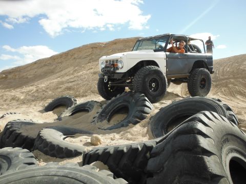 1979 Ford Bronco - A modified off-road vehicle navigates a sandy dune, with several large tires scattered in the foreground.