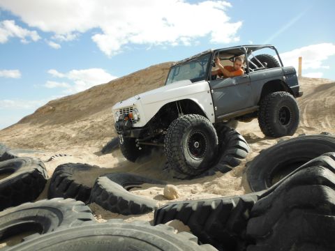 1979 Ford Bronco - A heavily modified off-road vehicle navigates a challenging sandy terrain littered with old tires.