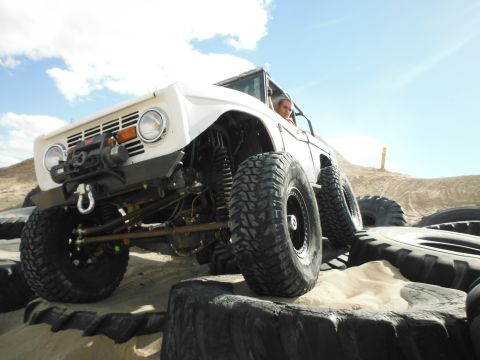 1979 Ford Bronco - Modified off-road SUV with oversized tires navigates a tire obstacle course under a clear sky.