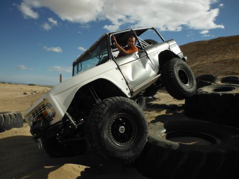 1979 Ford Bronco - A white 1979 Ford Bronco navigates an obstacle course of tires, with the driver giving a wave.