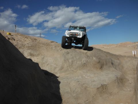 1979 Ford Bronco - A white off-road vehicle navigates a steep, sandy incline under a partly cloudy sky.