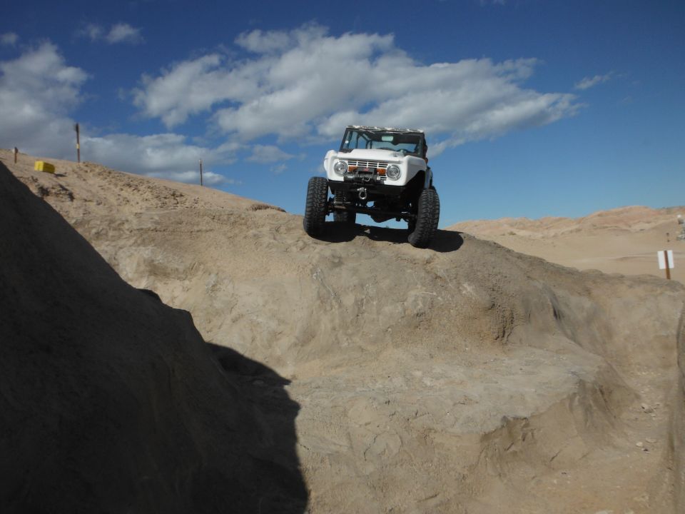 White Bronco climbing a dirt hill, big tires, sunny day