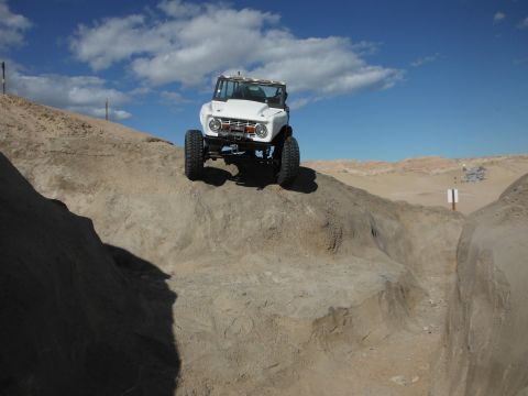 1979 Ford Bronco - A white off-road SUV navigates a steep dirt incline under a partly cloudy sky.