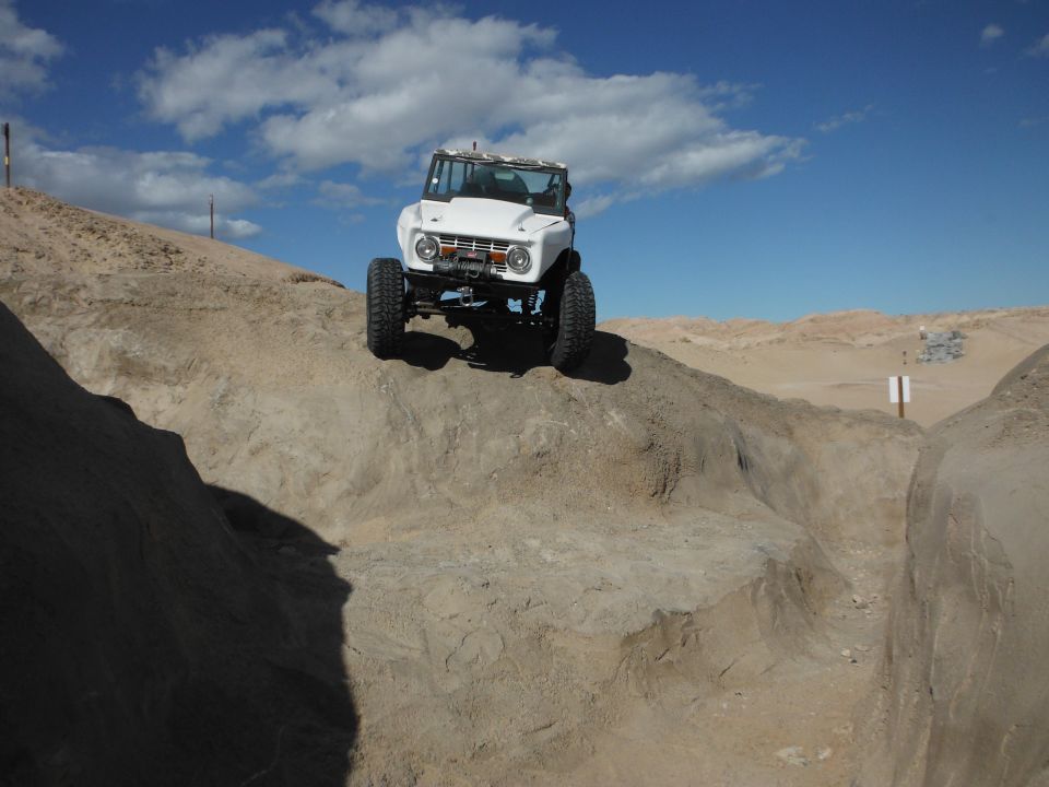 White off-road SUV with large tires on a dirt hill, front view