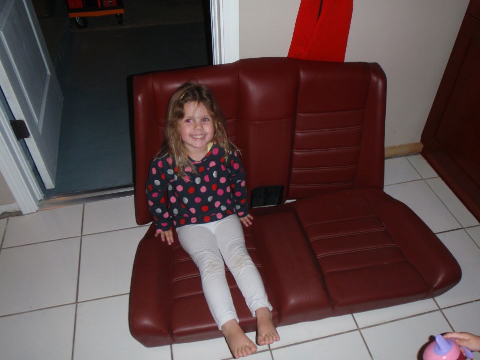 Young girl sits on a red car seat in a garage