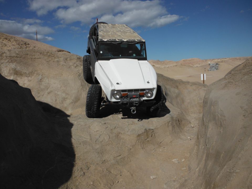White off-road vehicle with camouflage soft top climbing over rocks. Winch mounted on front