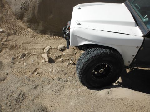 1979 Ford Bronco - Off-road tire and fender detail on a 1979 Ford Bronco navigating a rocky, sandy terrain.