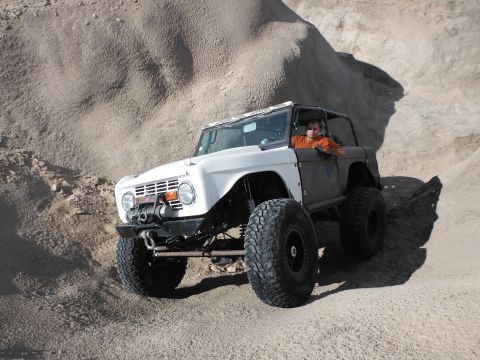 1979 Ford Bronco - This modified 1979 Ford Bronco navigates a sandy, hilly terrain with its driver visible behind the wheel.