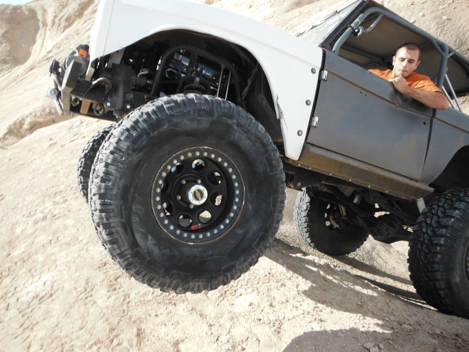 Modified SUV with large tires climbing a dirt hill, driver visible in cab