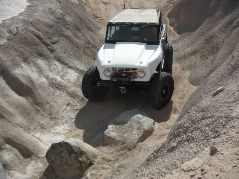 1979 Ford Bronco - A white off-road SUV tackles a challenging rocky and sandy path.