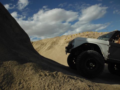 1979 Ford Bronco - A modified off-road vehicle navigates a sandy terrain under a cloudy sky.