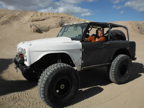 1979 Ford Bronco - A heavily modified 1979 Ford Bronco navigates sandy terrain under a cloudy sky.