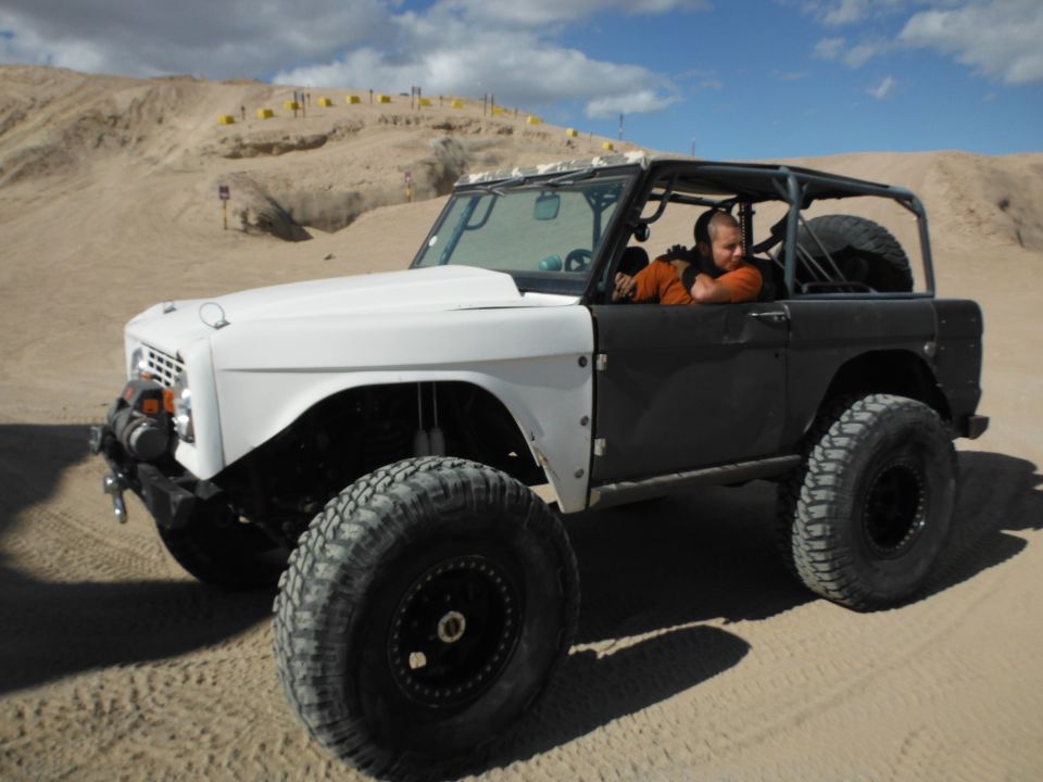 Modified 1979 Ford Bronco with a white hood and black body, off-roading in a sandy desert