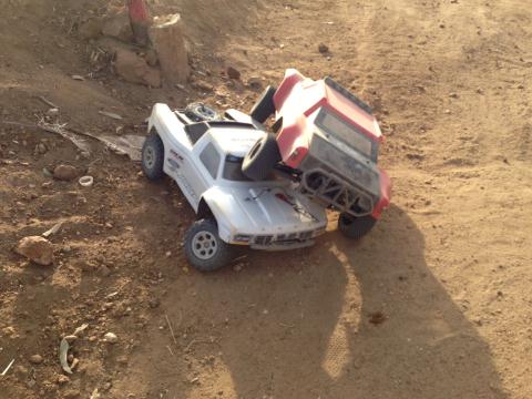 1986 Ford Bronco - RC trucks collided on a dirt track, with one on top of the other.