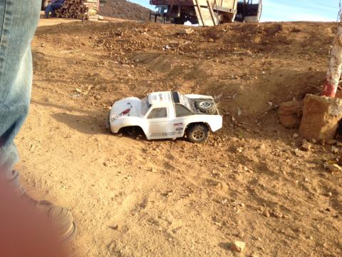 1986 Ford Bronco - A white remote control truck sits on a dirt track, with a person's legs in the foreground.