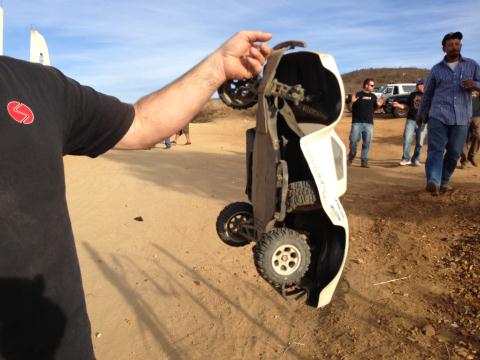 1986 Ford Bronco - A person holds up a white remote control car in a desert-like environment with other people and vehicles visible.