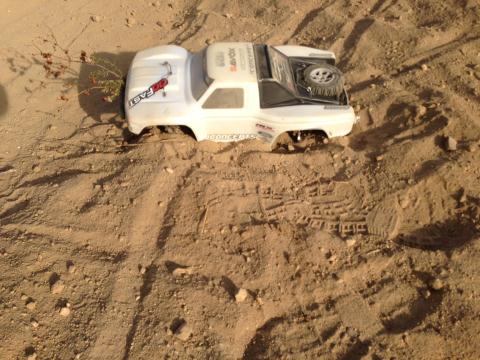 1986 Ford Bronco - A remote control truck body is partially buried in the sand, showing a spare tire mounted on the roof.