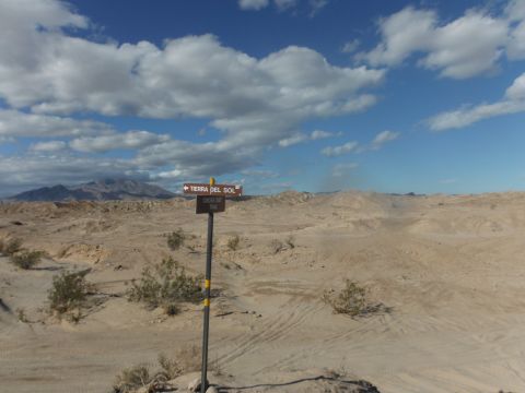 1979 Ford Bronco - A signpost stands in a vast, arid desert landscape under a cloudy blue sky.
