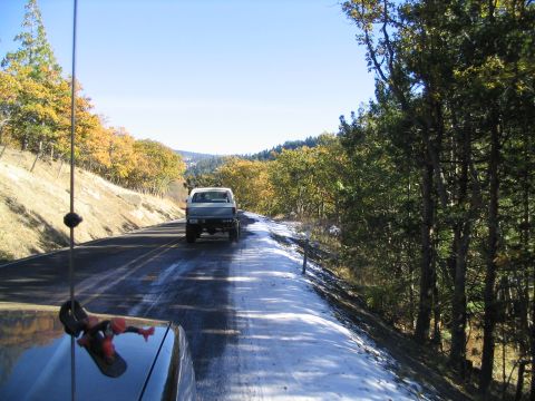 1988 Ford Bronco - A white pickup truck travels down a road with patches of snow and autumn leaves visible.
