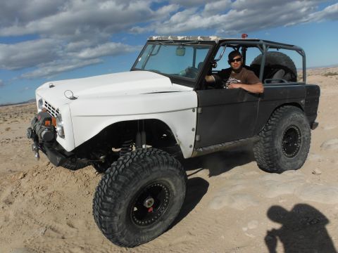 1979 Ford Bronco - A modified Ford Bronco with off-road tires sits in a desert landscape under a cloudy sky.