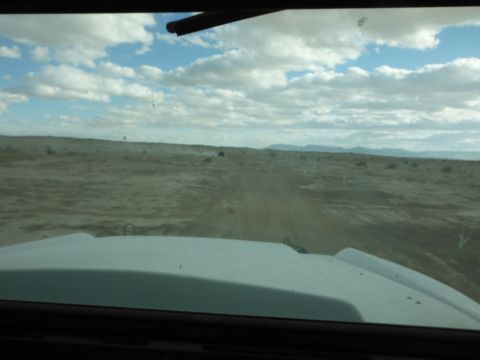 1979 Ford Bronco - Driving through a dusty, arid terrain with mountains in the distance under a partly cloudy sky.