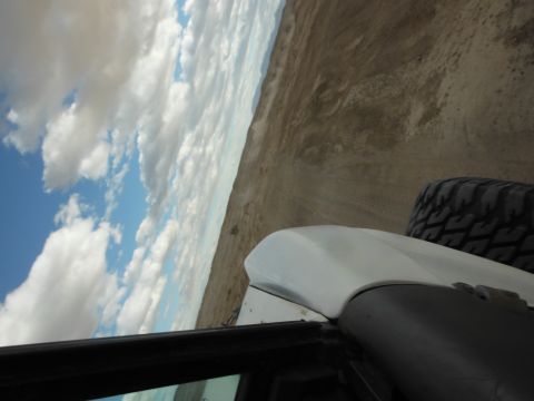 1979 Ford Bronco - View from inside a vehicle shows a white fender and tire against a desert landscape under a cloudy sky.