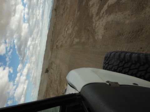 1979 Ford Bronco - View from inside a vehicle driving through a desert landscape under a cloudy sky.