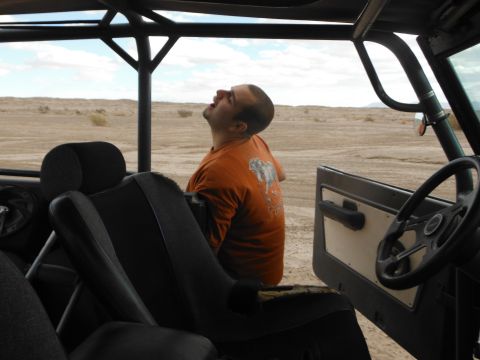 1979 Ford Bronco - Man looks up inside a vehicle with a roll cage, parked in a desert landscape.