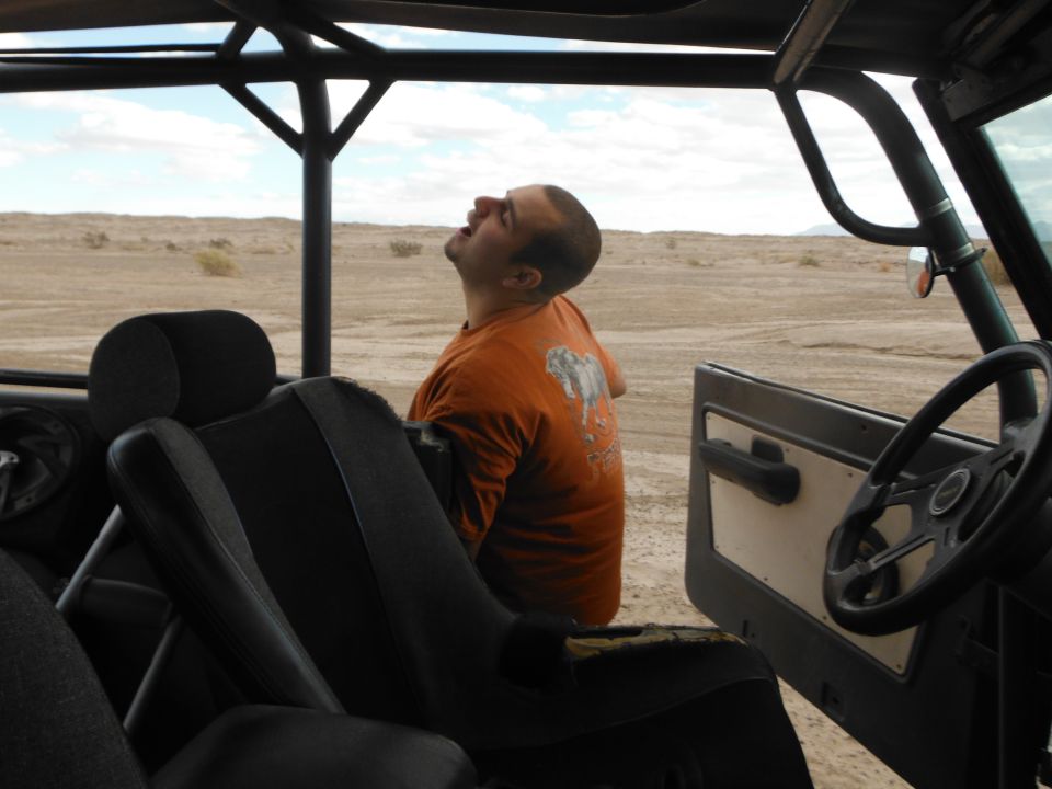 Interior of a vehicle with a man looking up, desert landscape visible through the open door