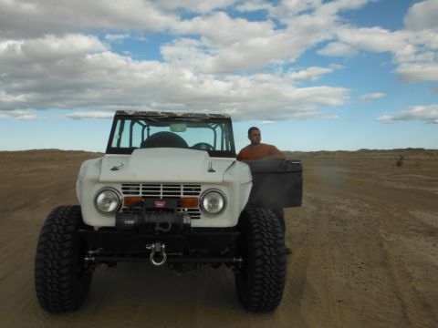 1979 Ford Bronco - White Ford Bronco with winch and aftermarket wheels is driven by a man in an orange shirt.