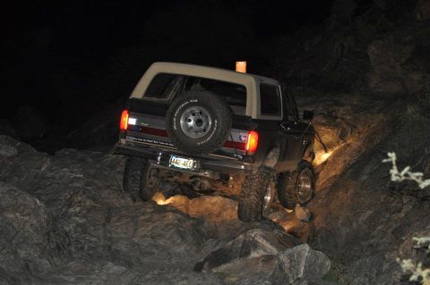 1991 Ford Bronco - A 1991 Ford Bronco is shown off-roading over rocks at night, with its rear end visible.