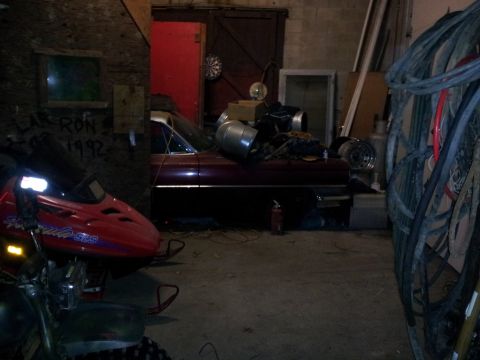 2006 Mitsubishi Evolution - A red snowmobile and a vintage car are stored in a messy garage with various items around.