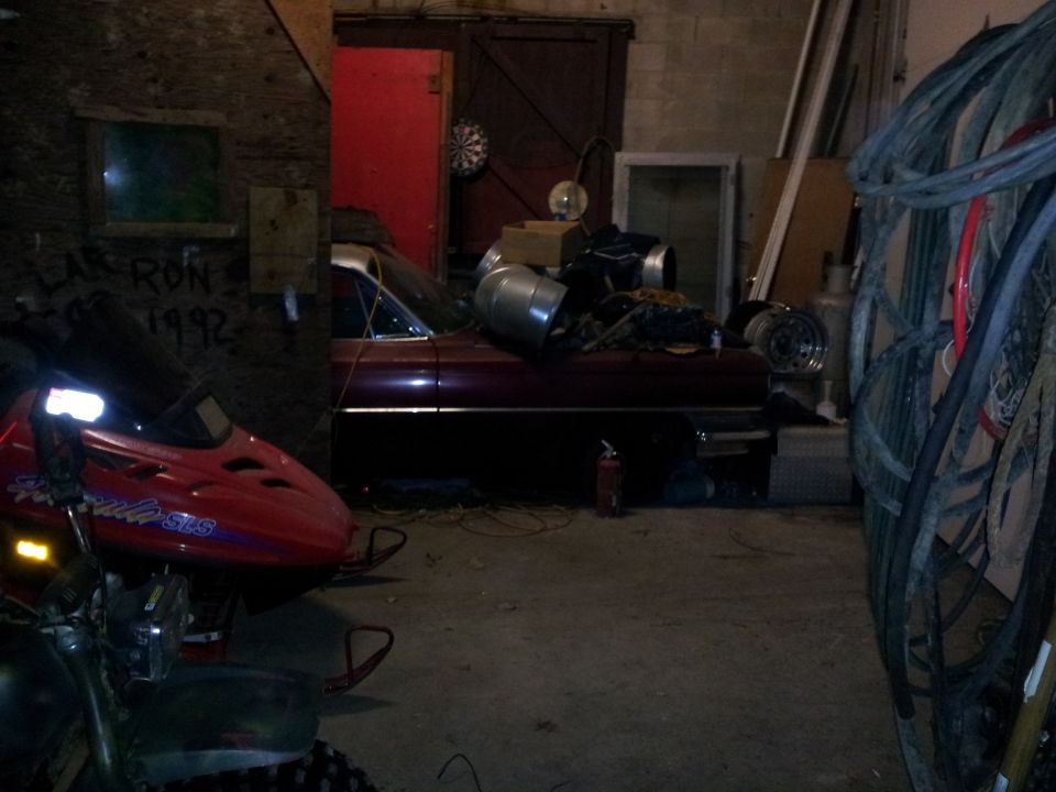Red snowmobile and a dark red vintage car parked inside a cluttered garage