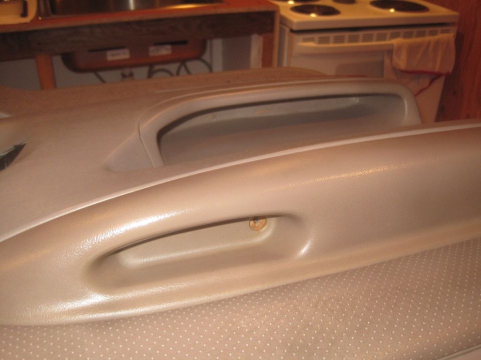 tan car door panel with a handle and a screw visible
