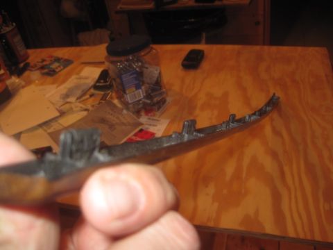 1993 Ford Bronco - A hand holds a dark, curved automotive trim piece with visible mounting clips against a wooden surface.