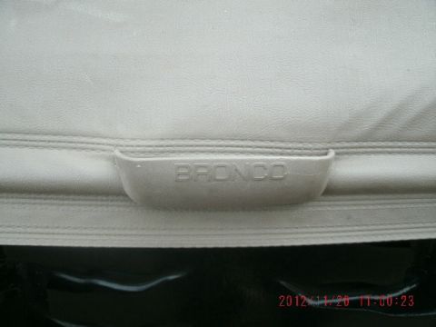 1994 Ford Bronco - Close-up of a light gray vinyl cargo cover or trim panel with a molded pull handle embossed 'BRONCO', laid on a black plastic surface outdo…