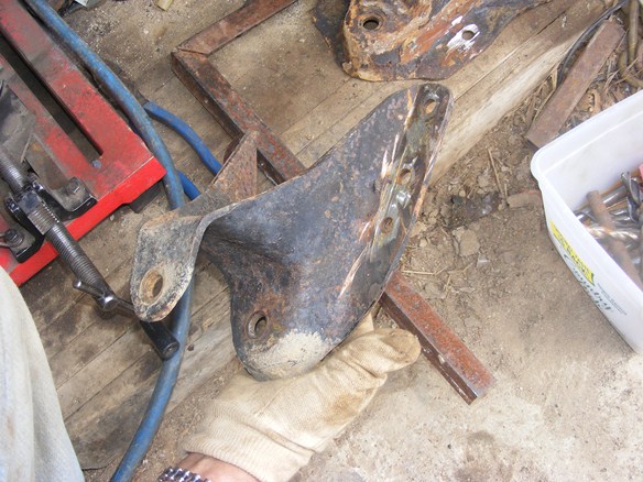 rusted metal bracket held by gloved hand, with tools and other metal parts in background