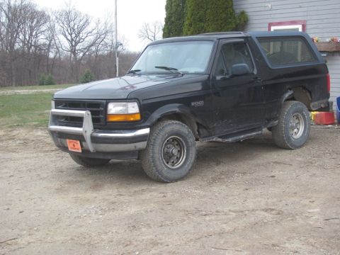 1996 Ford Bronco - A black 1996 Ford Bronco is parked outdoors on a dirt surface, showing its side and front quarter view.