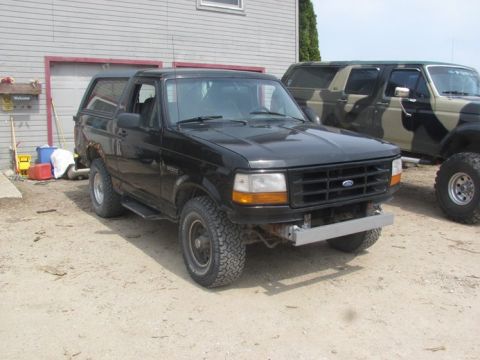 1996 Ford Bronco - A black 1996 Ford Bronco is parked in front of a garage, with another modified SUV visible behind it.