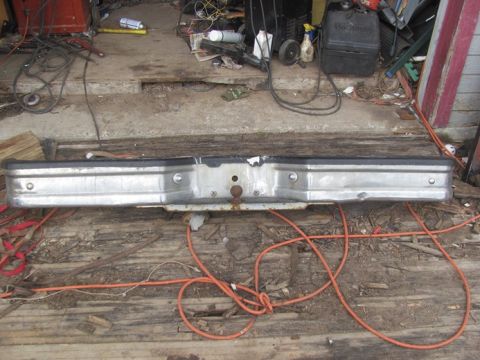 1996 Ford Bronco - A detached vehicle bumper, possibly for an older truck or SUV, rests on a weathered wooden floor amidst various tools and supplies.