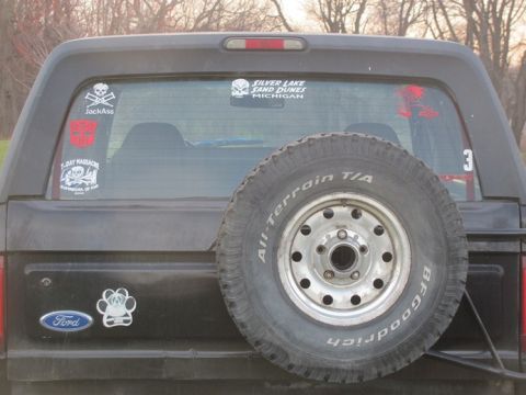1996 Ford Bronco - Rear view of a black Ford Bronco with a spare tire and decals on the window.