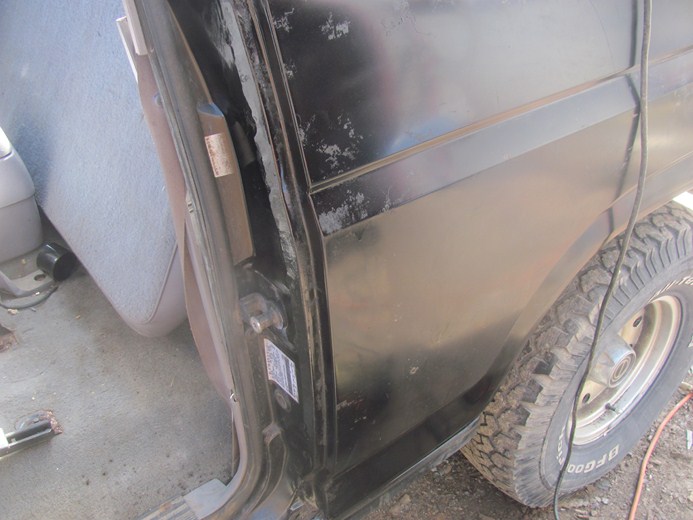 Interior shot of a black Ford Bronco showing the driver's seat and door jamb, with the rear quarter panel and tire visible